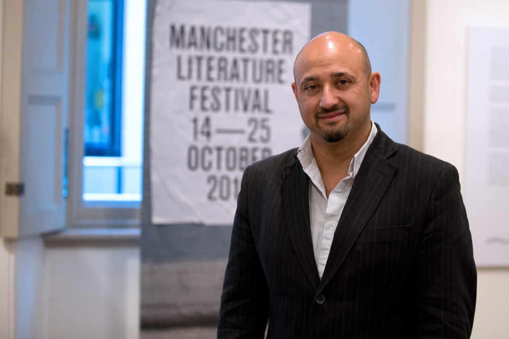 Portrait of John Siddique in front of festival banner