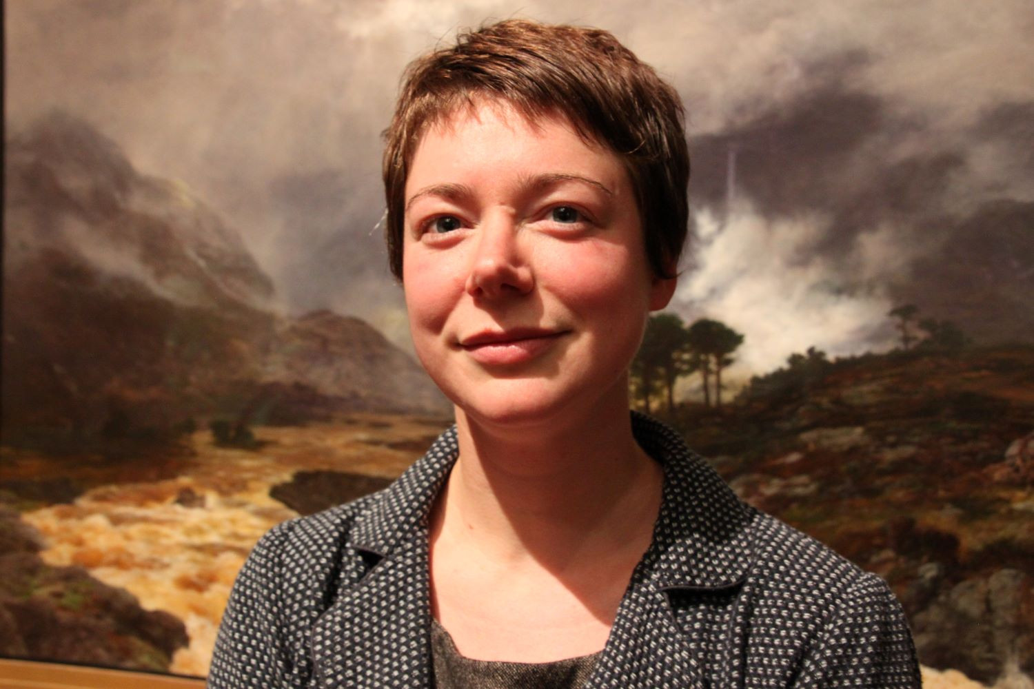 Portrait of Jen Hadfield in front of painting of the Scottish Highlands